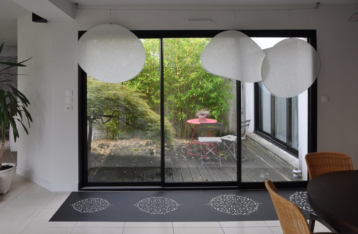 salon avec luminaires blancs, porte vitrée, tapis bleu gris donnant sur l'extérieur du projet de décoration intérieure Nantes 02 par la société de décoration intérieure deco.code dirigée par Sandrine Emery.