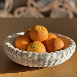 artisanal corbeille en rotin fabriqué à la main remplie d'oranges baignant dans la lumière du soleil, posée sur une table en bois naturel