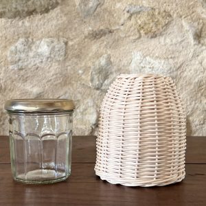Vase en rotin fait à la main et pot à confiture, tous deux posés sur une table en bois devant un mur en pierre naturelle.
